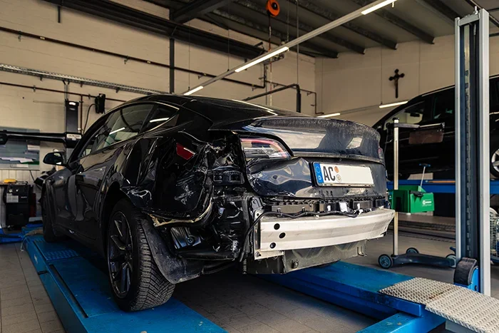 Ein Tesla mit Unfallschaden wird in der Werkstatt von Cremer & Sohn in Düren repariert, umgeben von weiteren Fahrzeugen, Werkzeugen und Ersatzteilen.